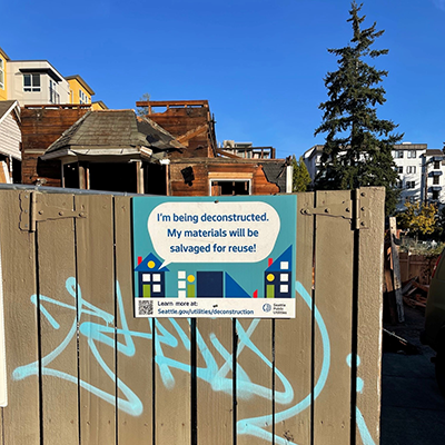 Photograph of house being deconstructed with signage on fence.