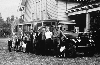 Black and white photo of residents of an early watershed settlement posing in front of an old bus, circa 1920s.