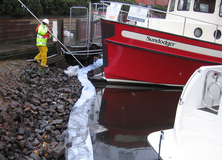 Spill Responders collect oil that is washing onto rocks after a large accident involving a truck spilled fuel into Lake Union.