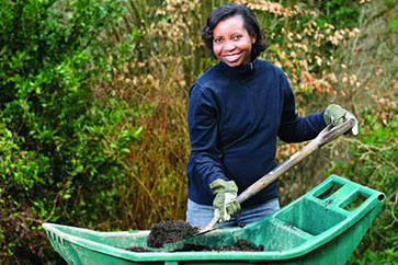 Woman with a shovel and wheelbarrow of compost.