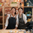 Two smiling business owners standing behind counter in coffee shop.