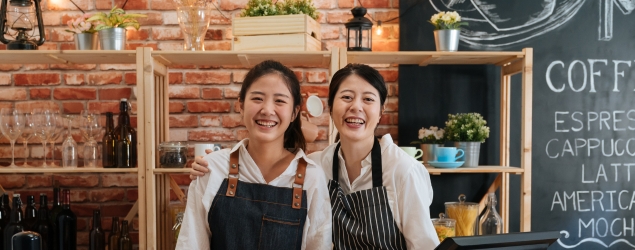 Two smiling business owners standing behind counter in coffee shop.