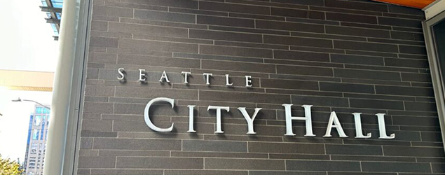 Exterior wall of Seattle City Hall with large metal letters spelling ‘Seattle City Hall’ mounted on dark brick.