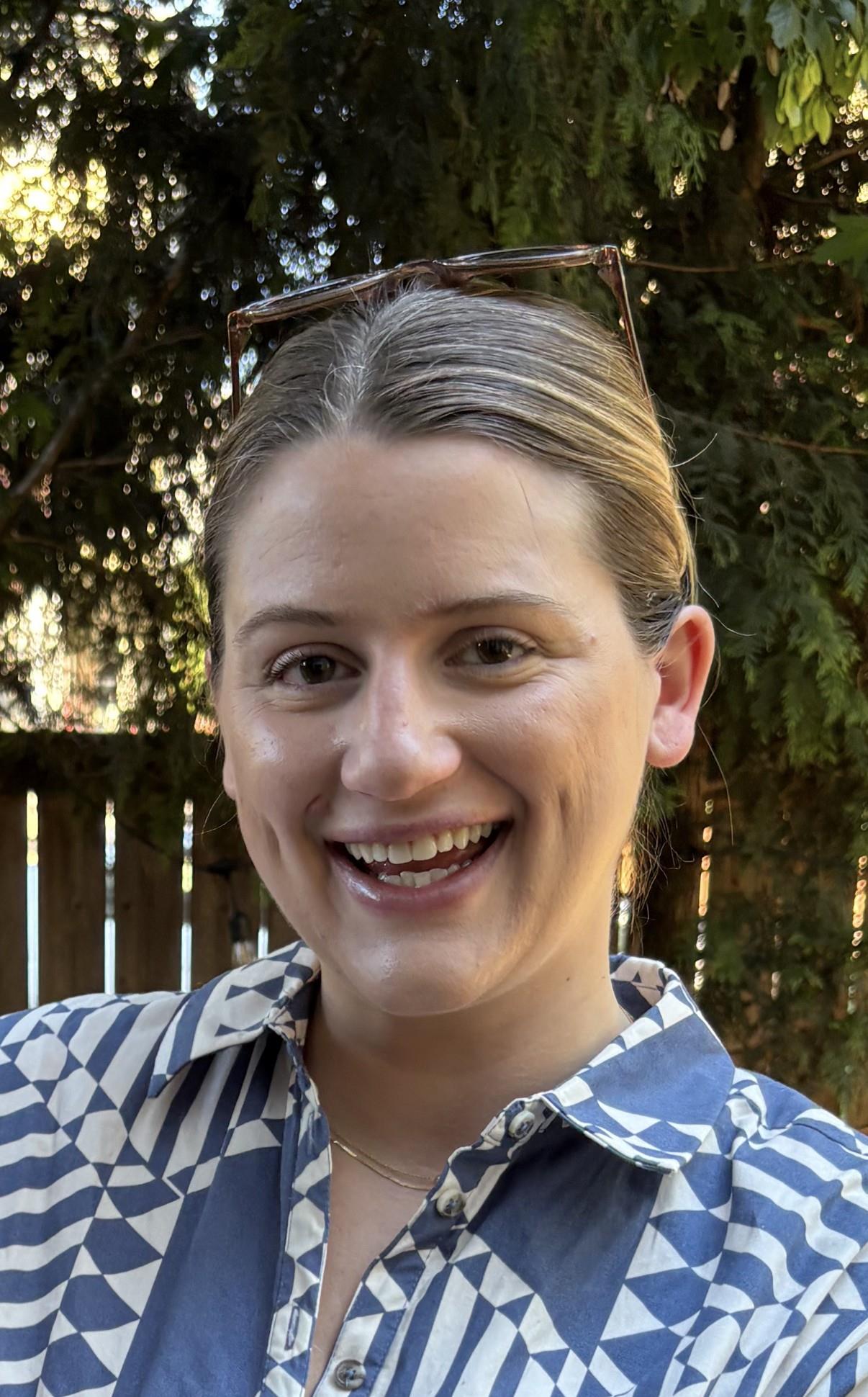 Portrait of Hailey smiling broadly at the camera in a patterned shirt with trees in the background