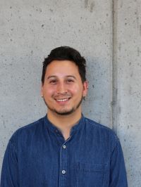 Dylan smiling at the camera in a dark blue button-up shirt in front of a grey background.